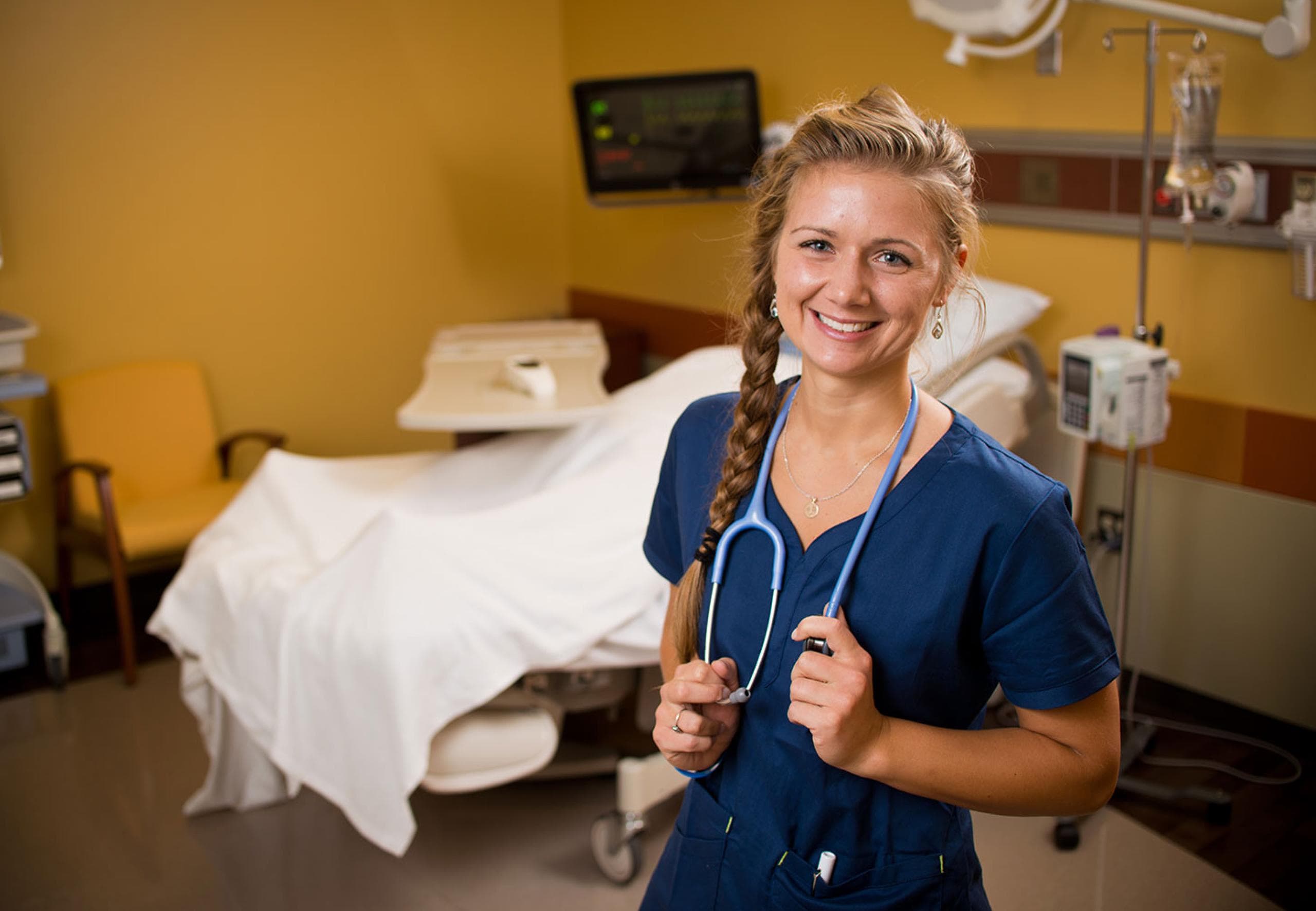 a nurse in front of a hospital bed smiling at the camera